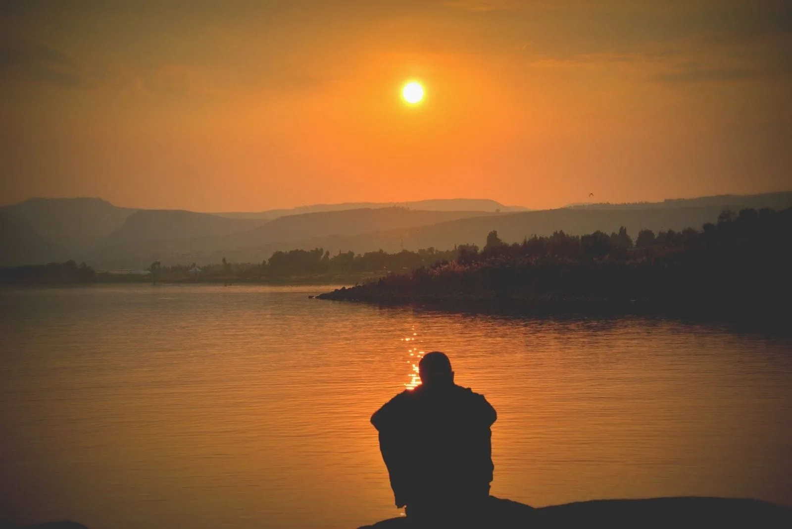 silhouette of a person sitting near the lake with the moon above