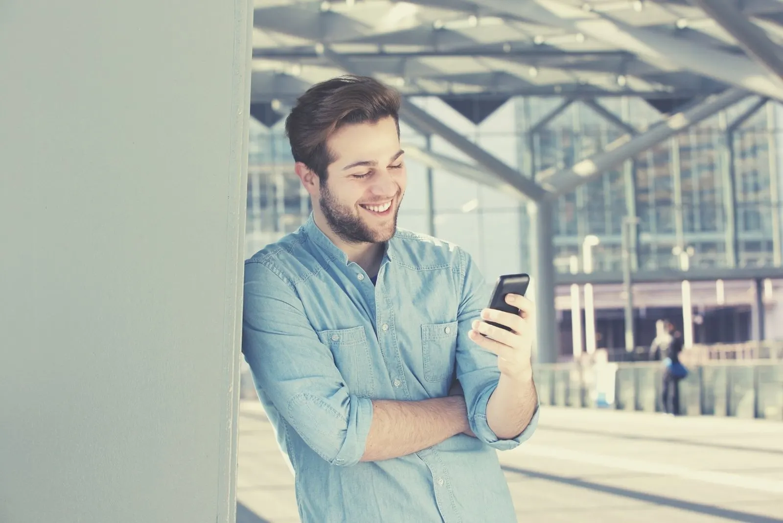 smiling office man reading text messages from his cellphone standing and leaning on the walls