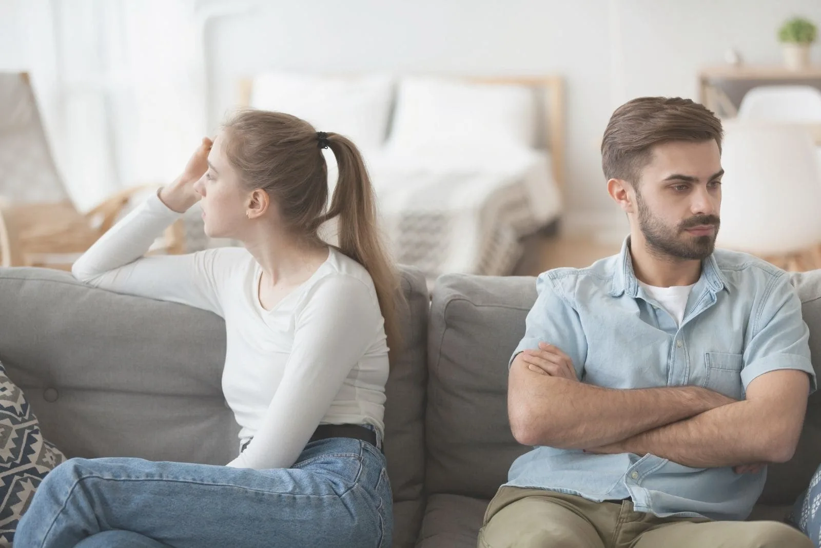 stubborn couple sit on couch separately to avoid talking after a fight
