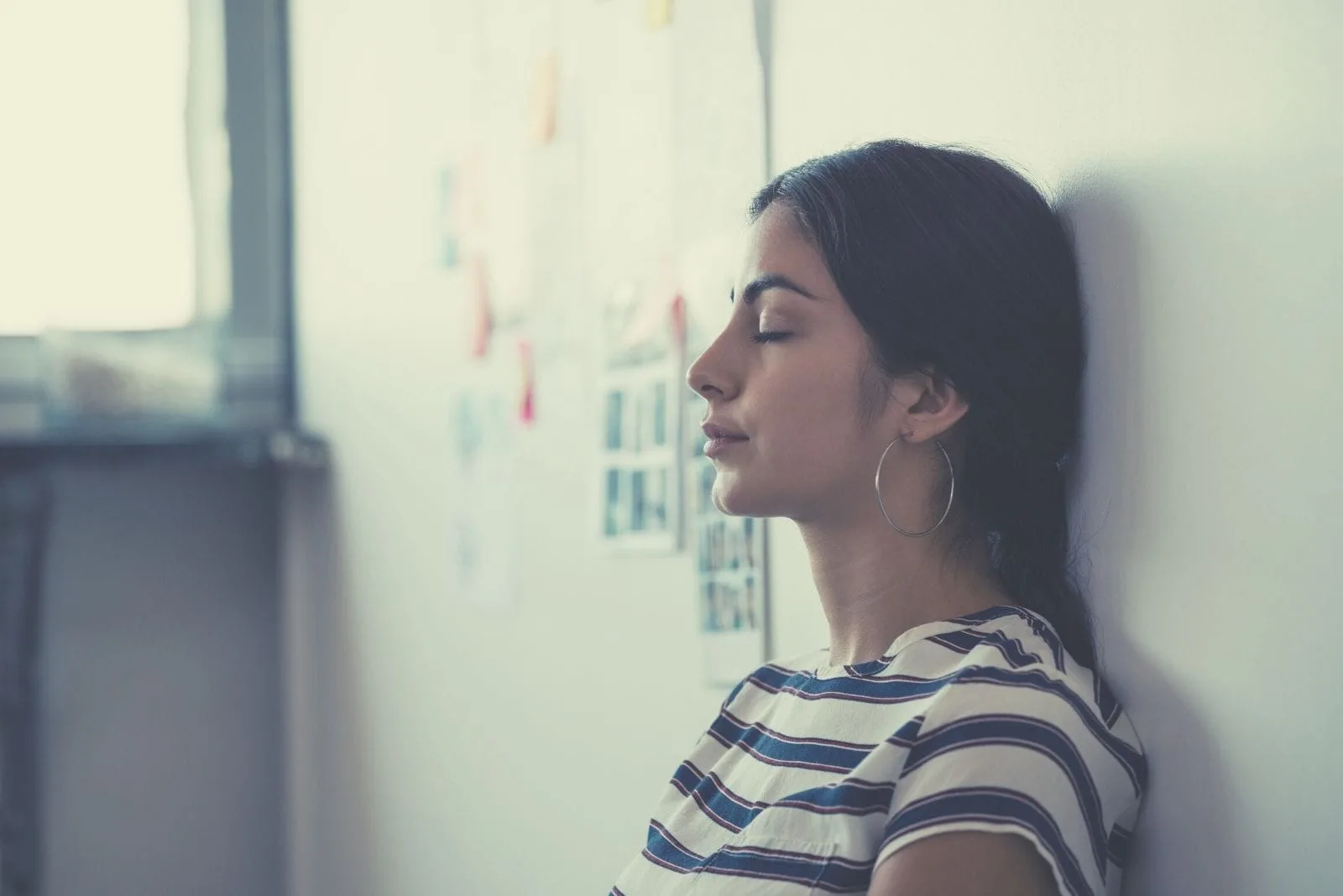 tired woman leaning on the wall inside the office and closing her eyes