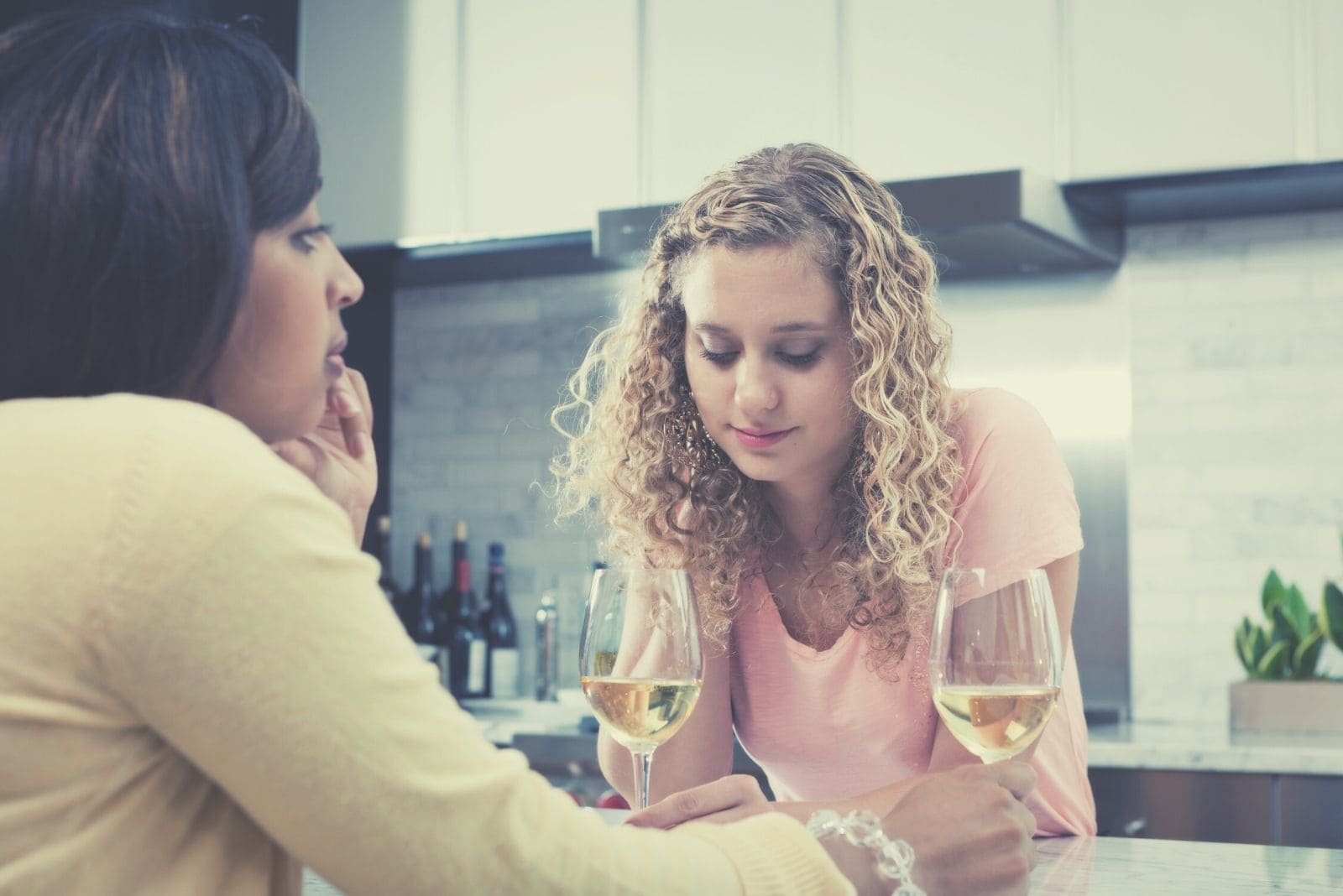two women friends talking seriously in the kitchen while drinking wine
