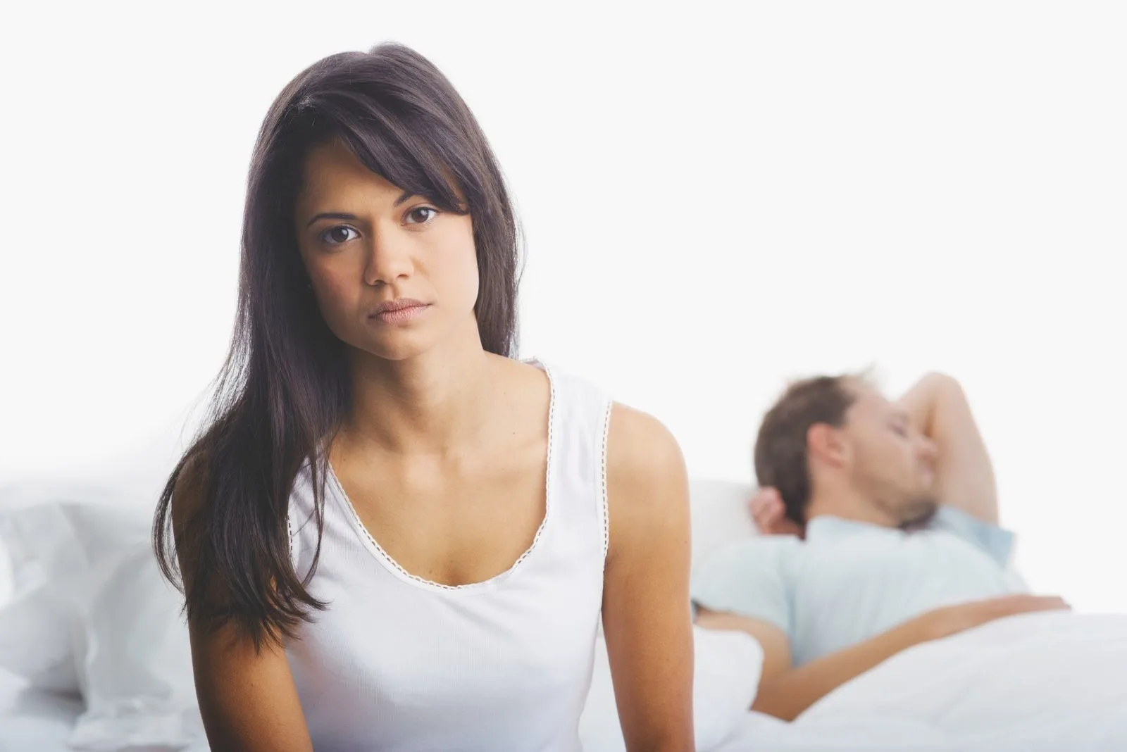upset woman sitting in bed with a man sleeping in the background