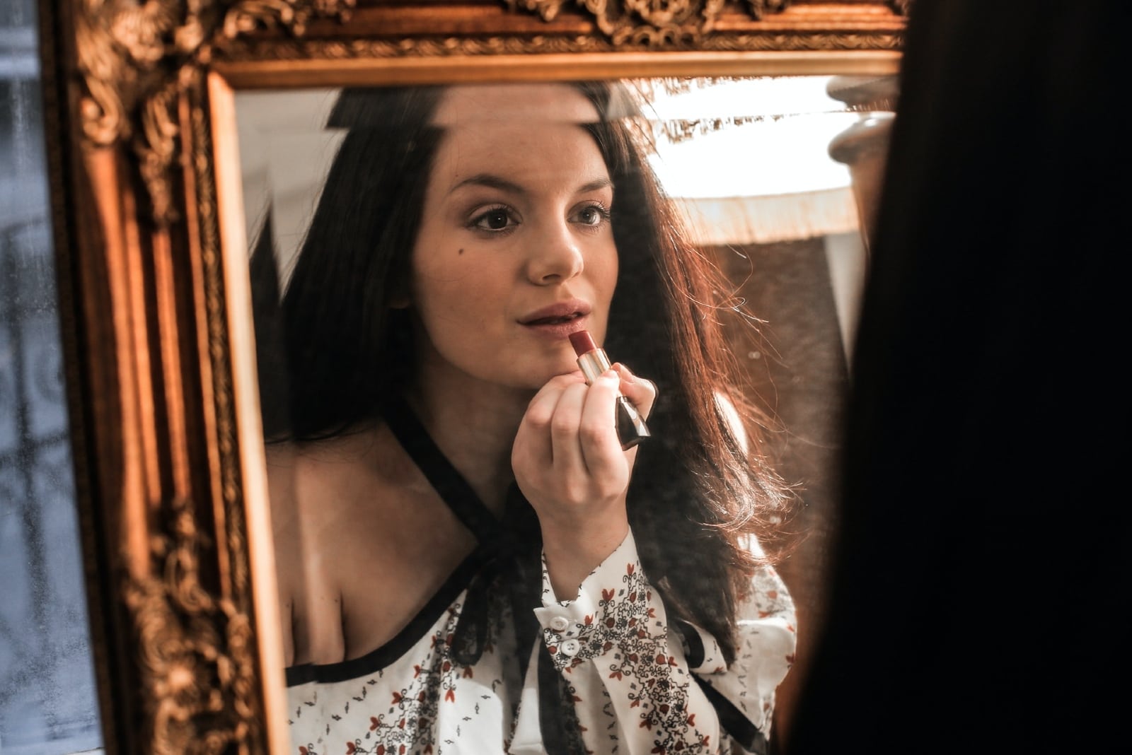 woman applying lipstick while looking in the mirror