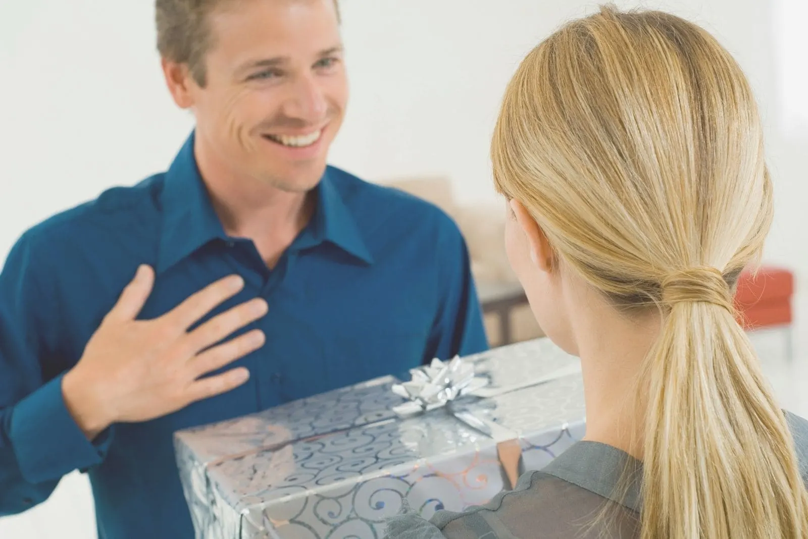 woman giving gift covered with silver wrapper to a surprised man