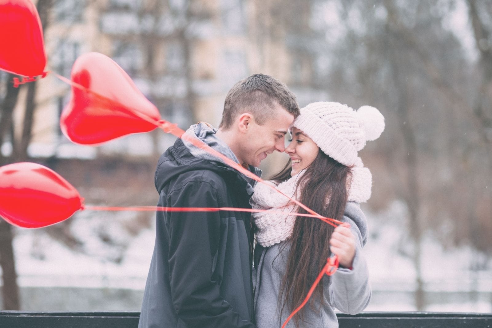 woman holding heart shaped balloons while with boyfriend standing outdoors