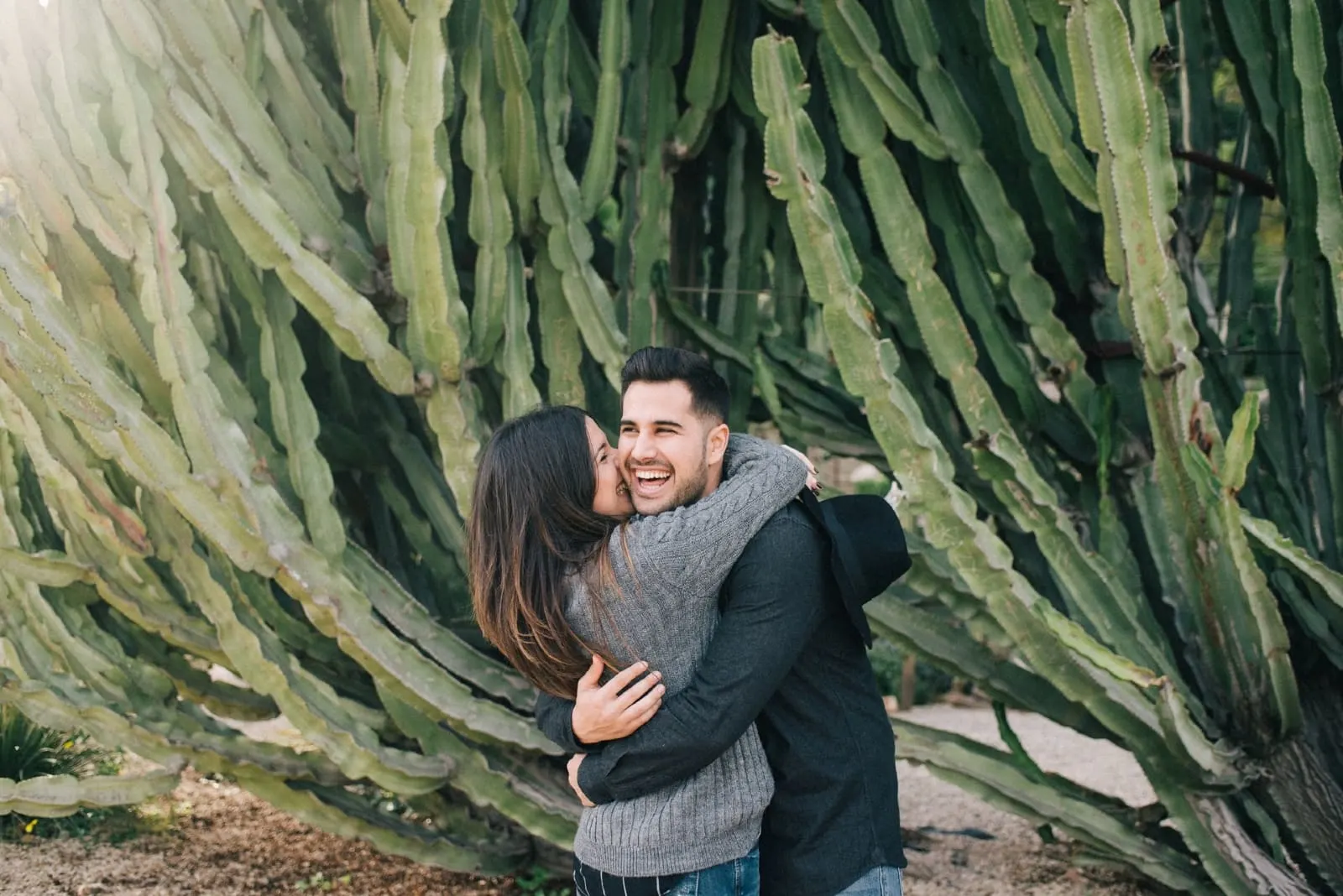 woman kissing man while standing near cactus