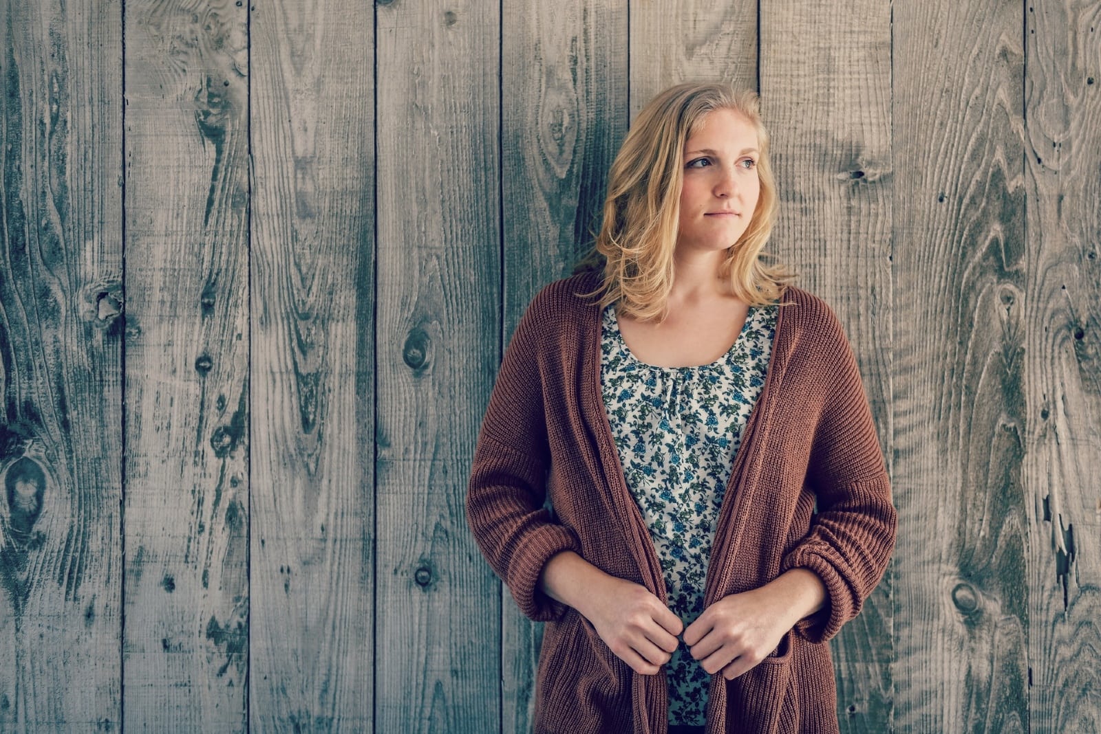 woman in brown cardigan leaning on wooden wall