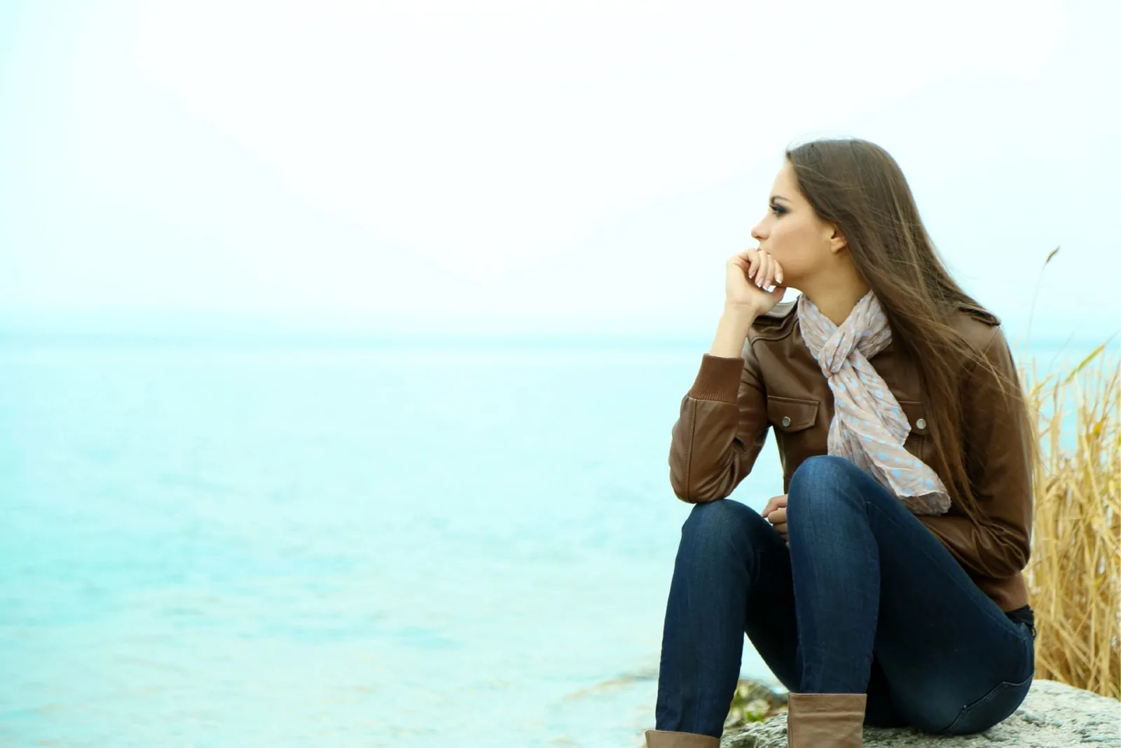 pensive woman in brown jacket sitting near water