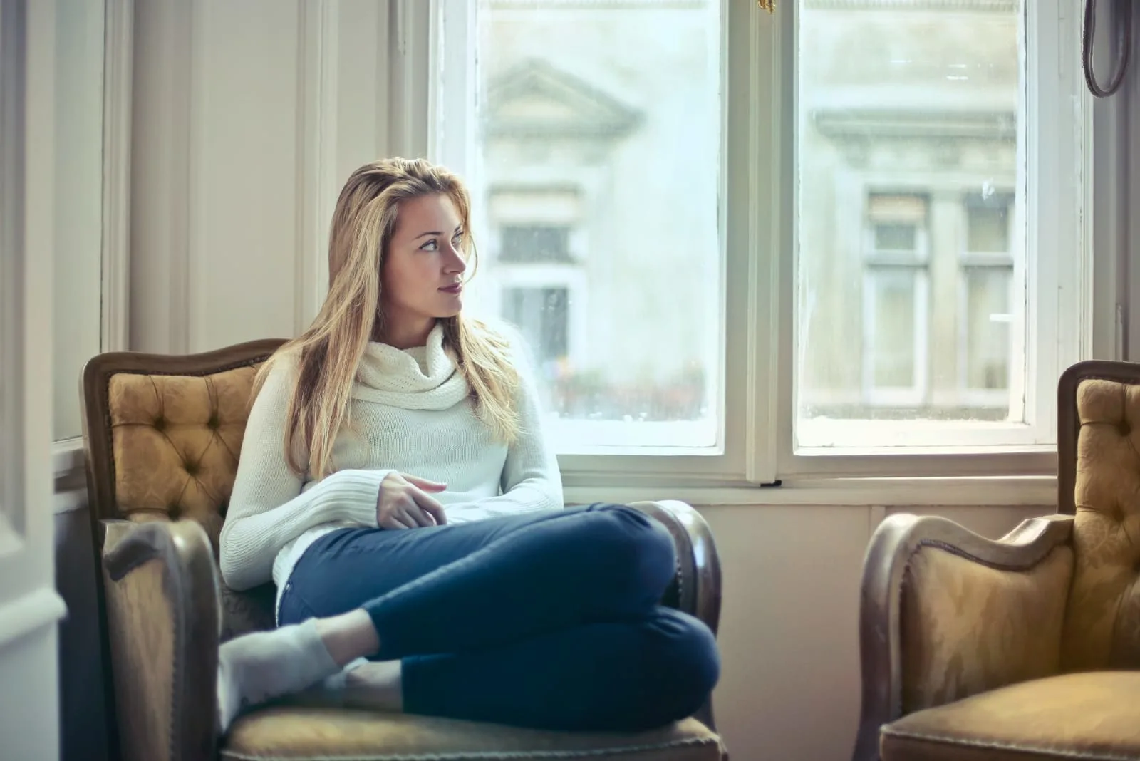 blonde woman sitting on armchair near window