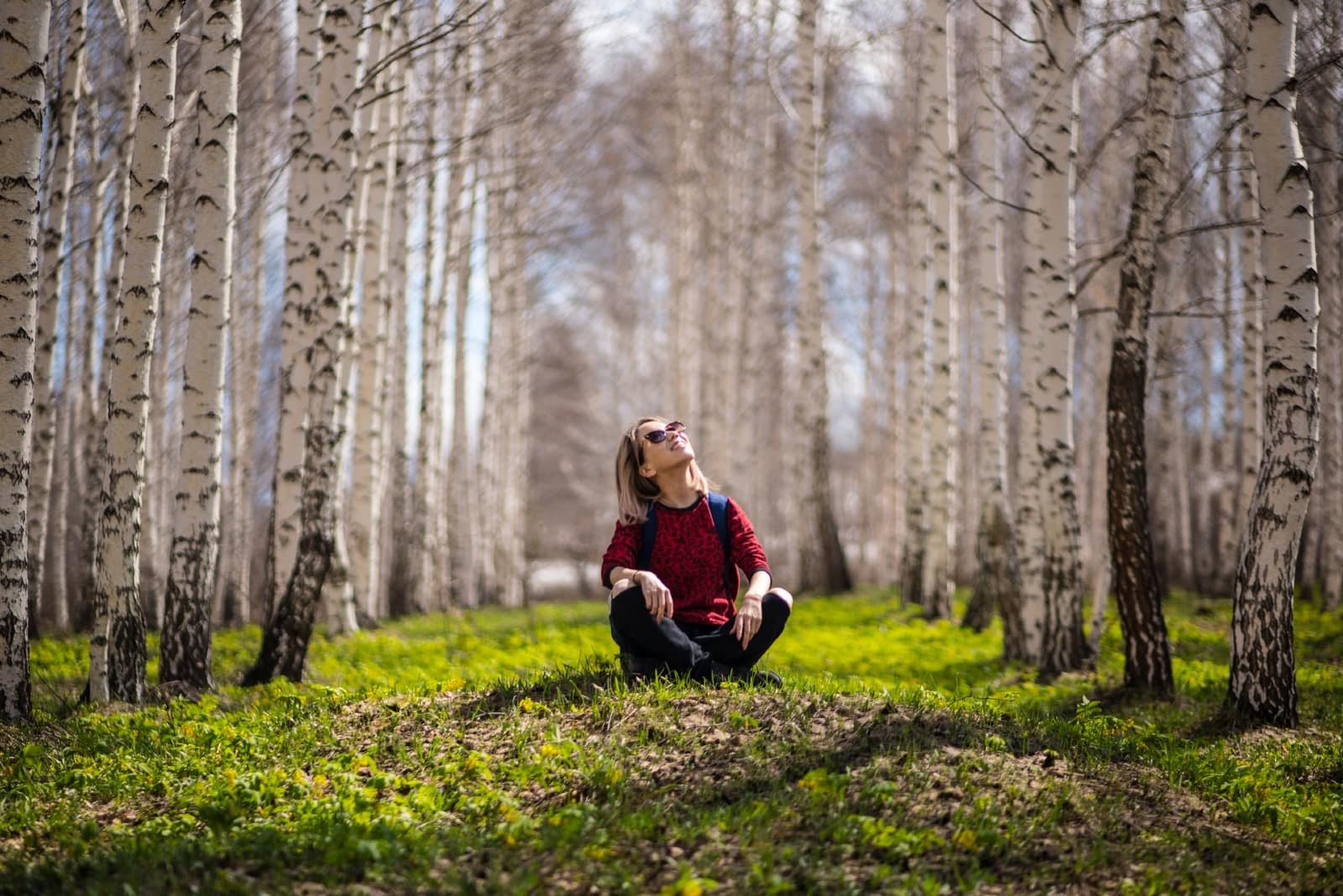 happy woman with backpack sitting on ground near trees
