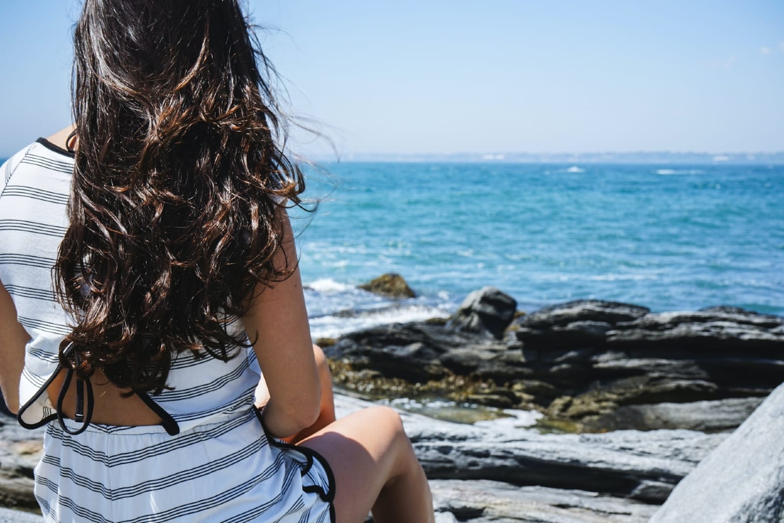 mujer sentada en una roca mirando al mar