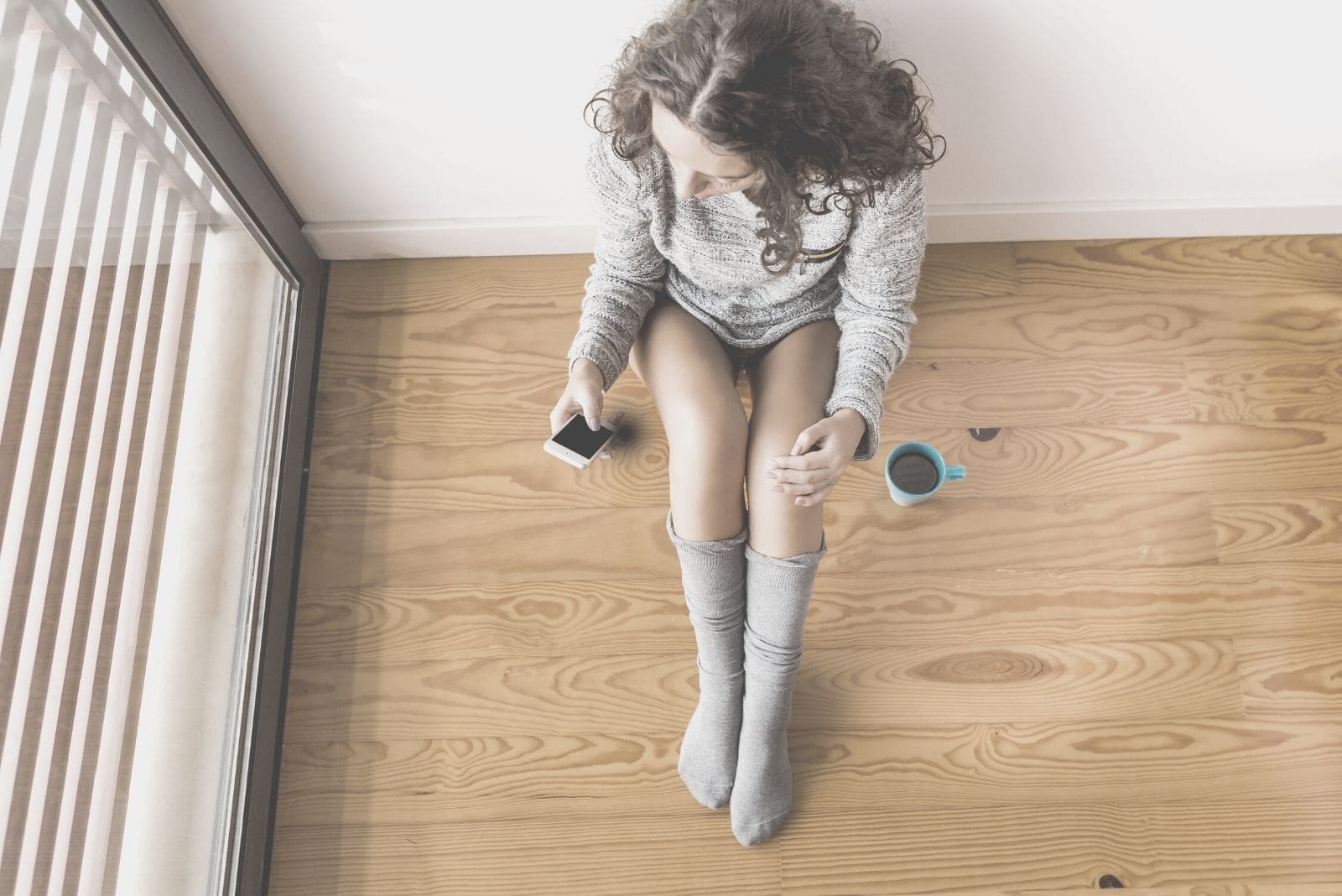 woman sitting on the floor drinking coffee and texting on top angle