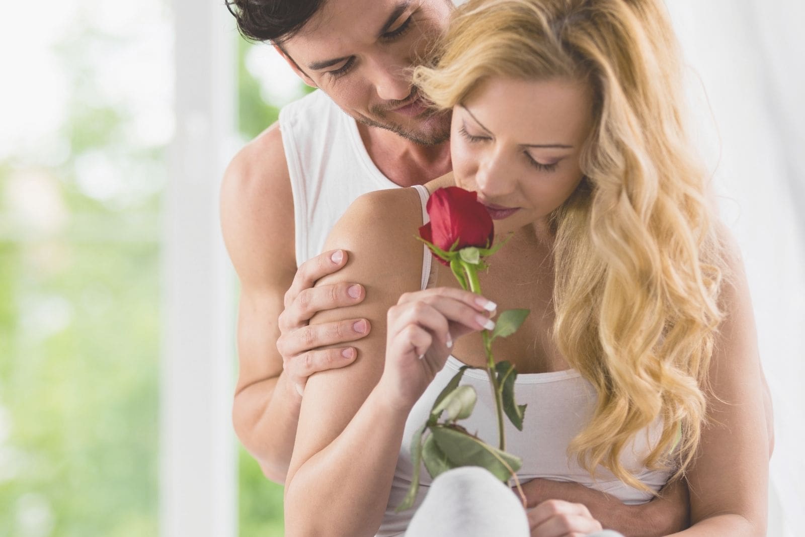 mujer que huele una rosa regalada por su romántico marido que la abraza