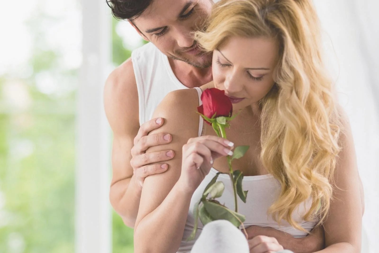 woman smelling a rose given by his romantic husband hugging her