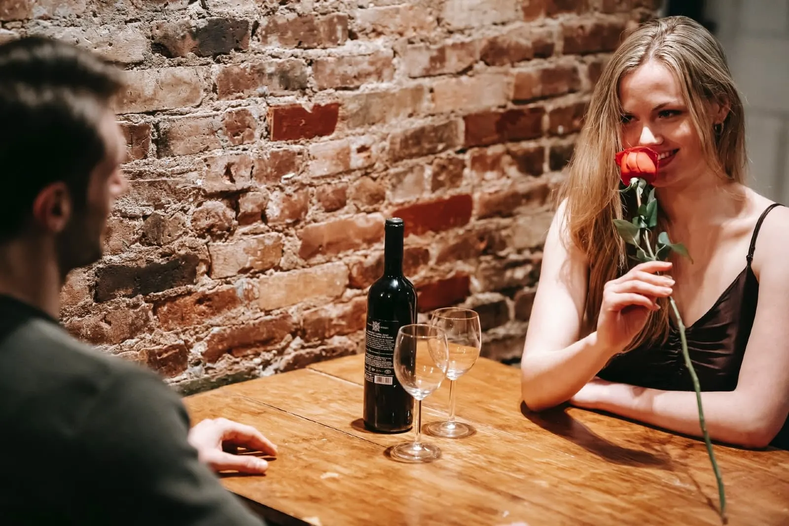 woman smelling red rose while sitting at table