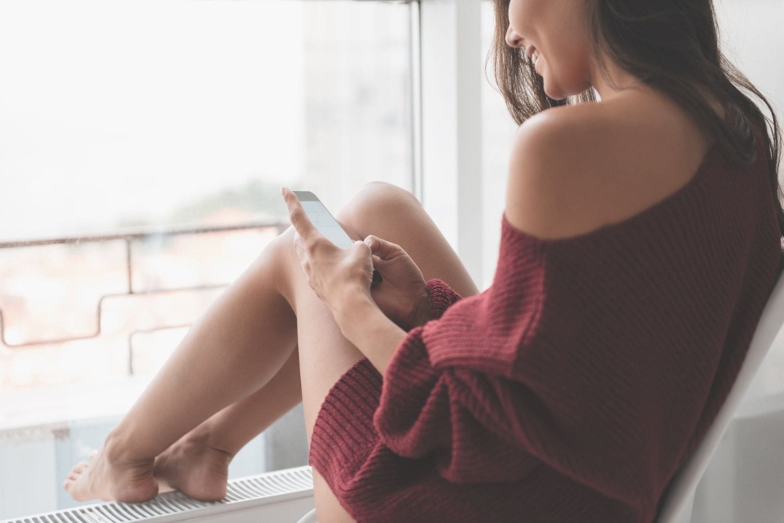 woman smiling and texting while sitting in the window sill in cropped image