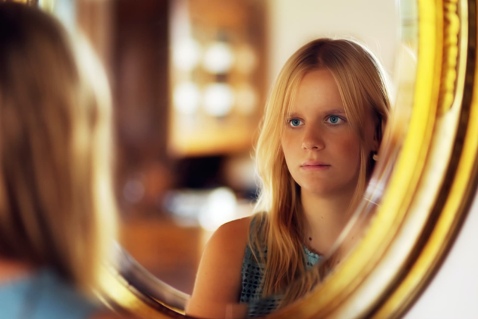 blonde woman ij blue top standing in front of mirror