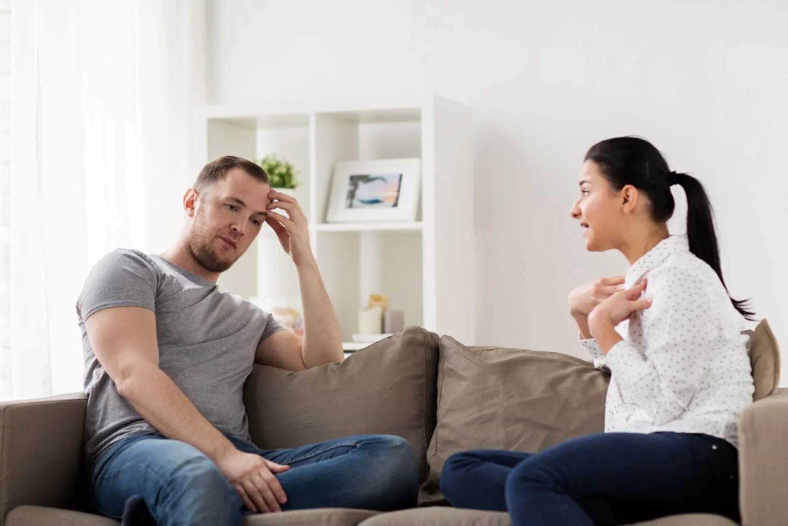 angry woman talking to man while sitting on sofa