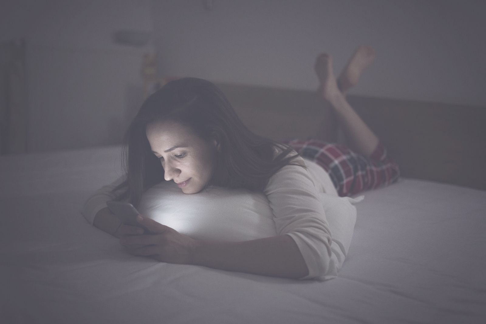 woman texting in bed while lying in bed in a dark room