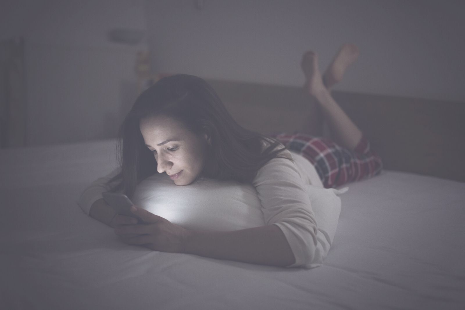 mujer enviando mensajes de texto en la cama mientras está acostada en una habitación oscura