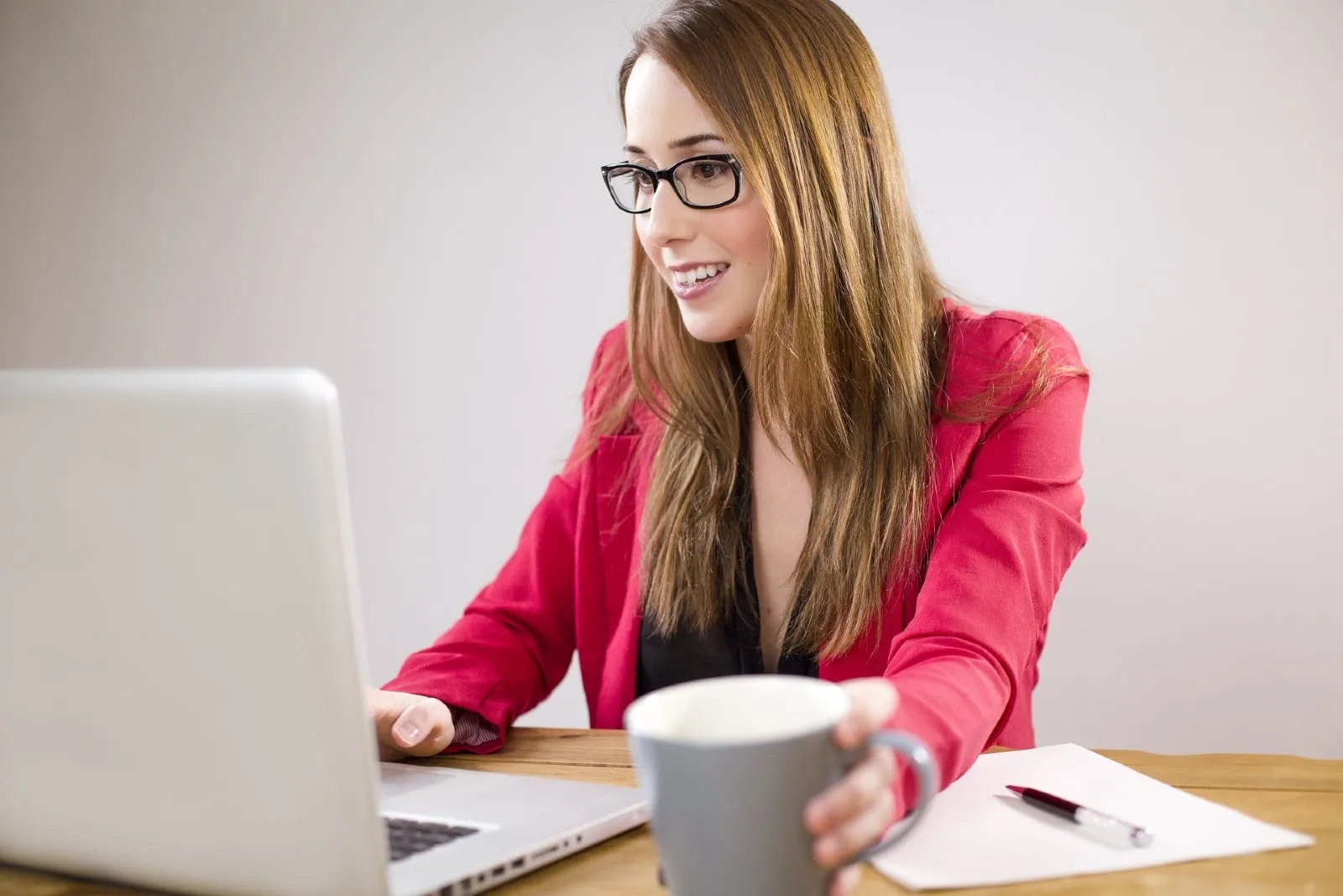 woman using laptop while holding gray mug