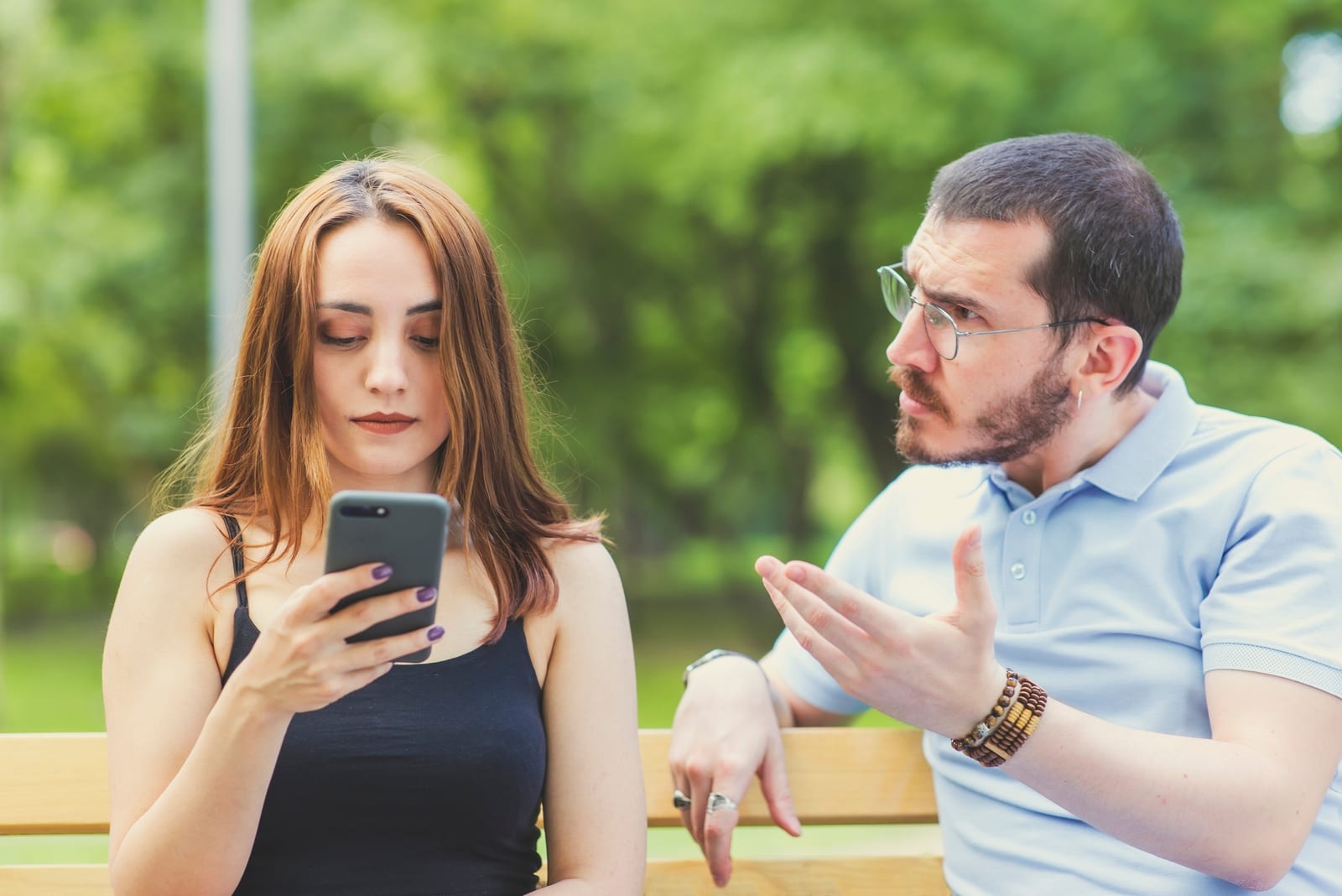 woman using smartphone while sitting near angry man