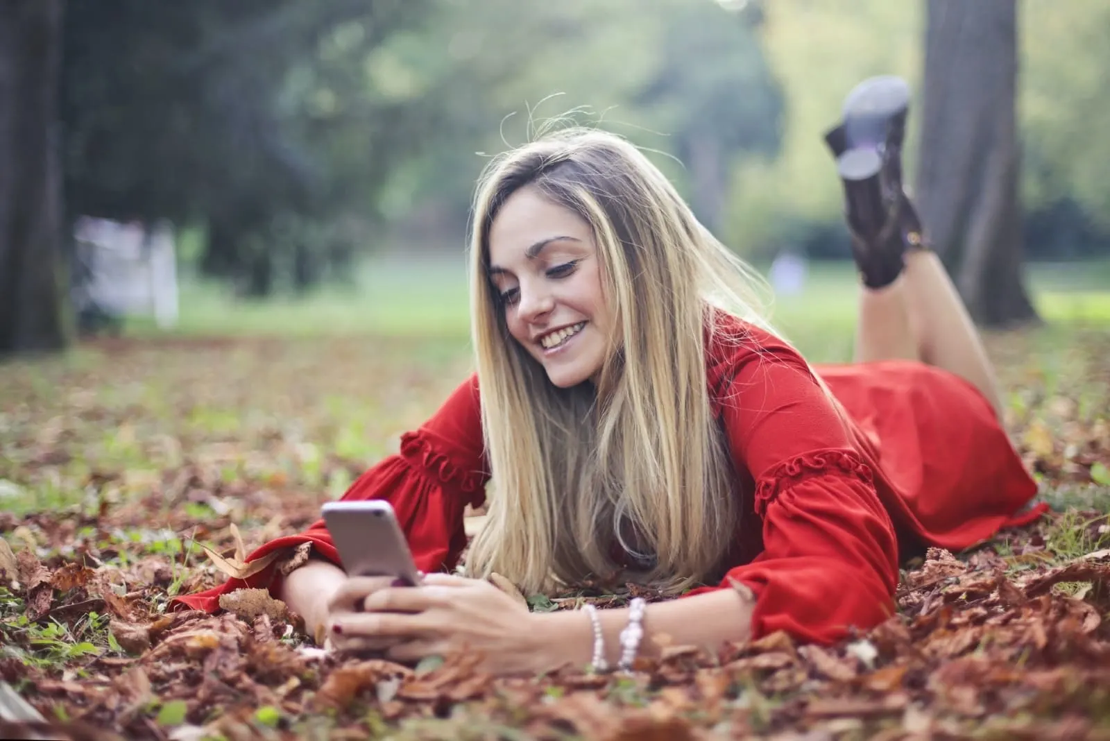 blonde woman using smartphone while laying on leaves