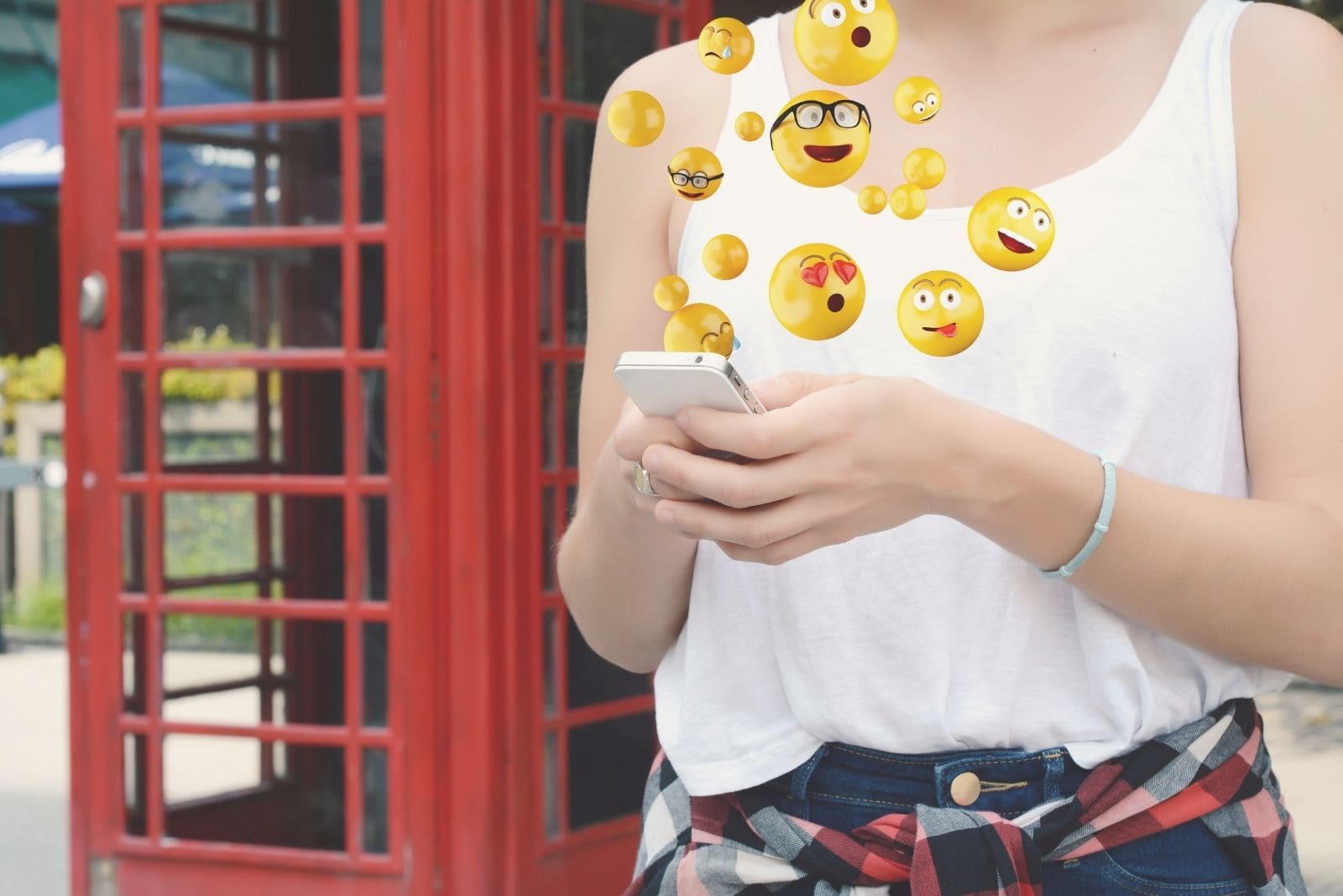 woman using smartphone sending emojis standing outside of a cafe in cropped image