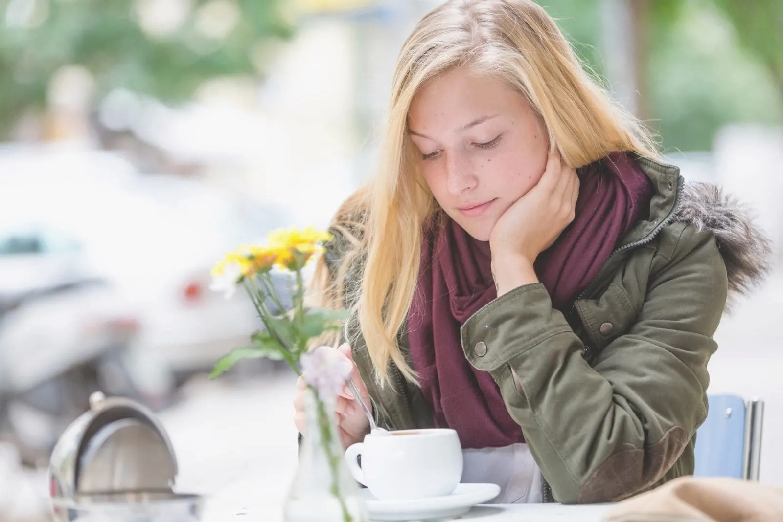 woman waiting in cafe outside lost in thoughts and mixing her coffee 