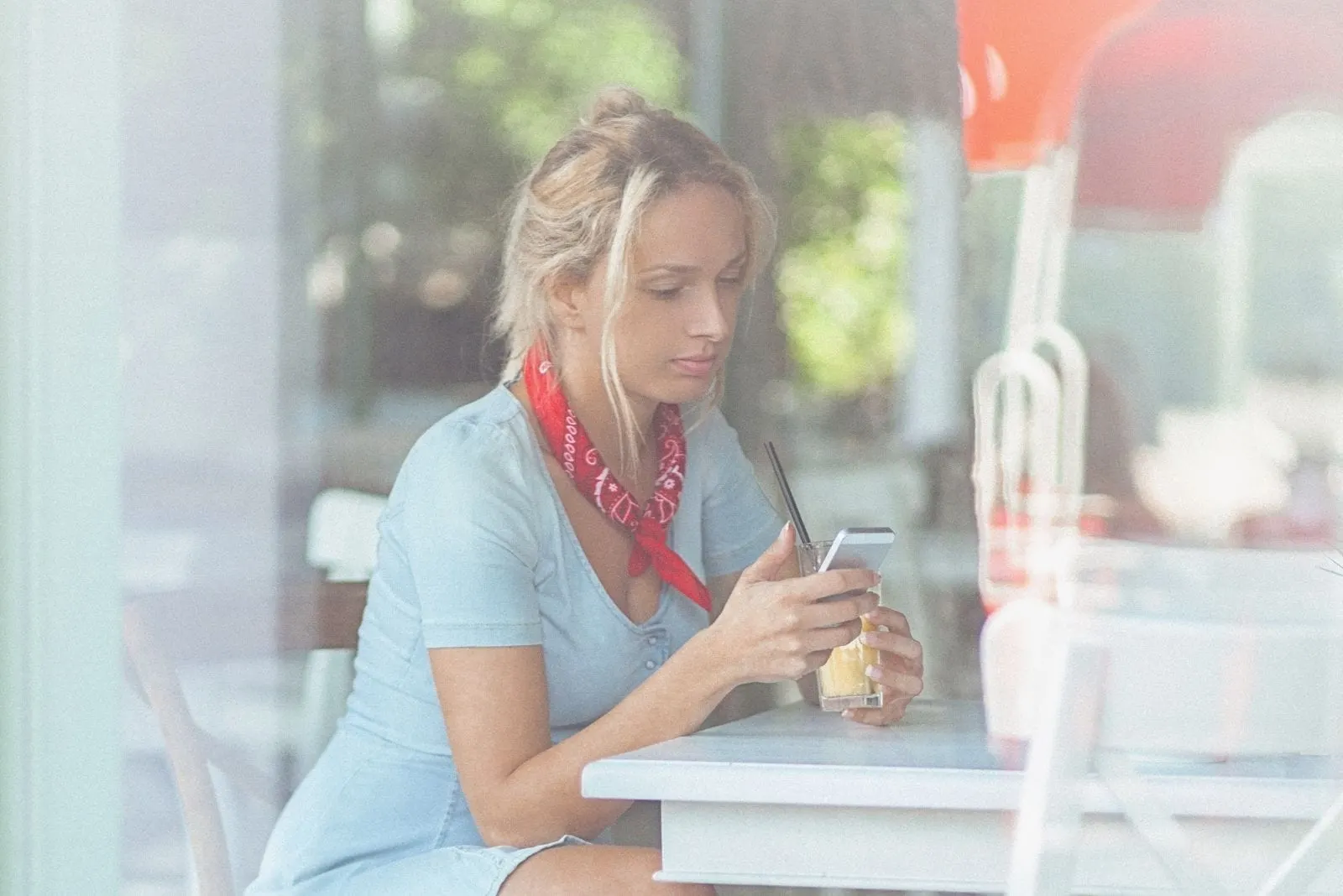 woman with a red scarf texting in her phone inside a cafe
