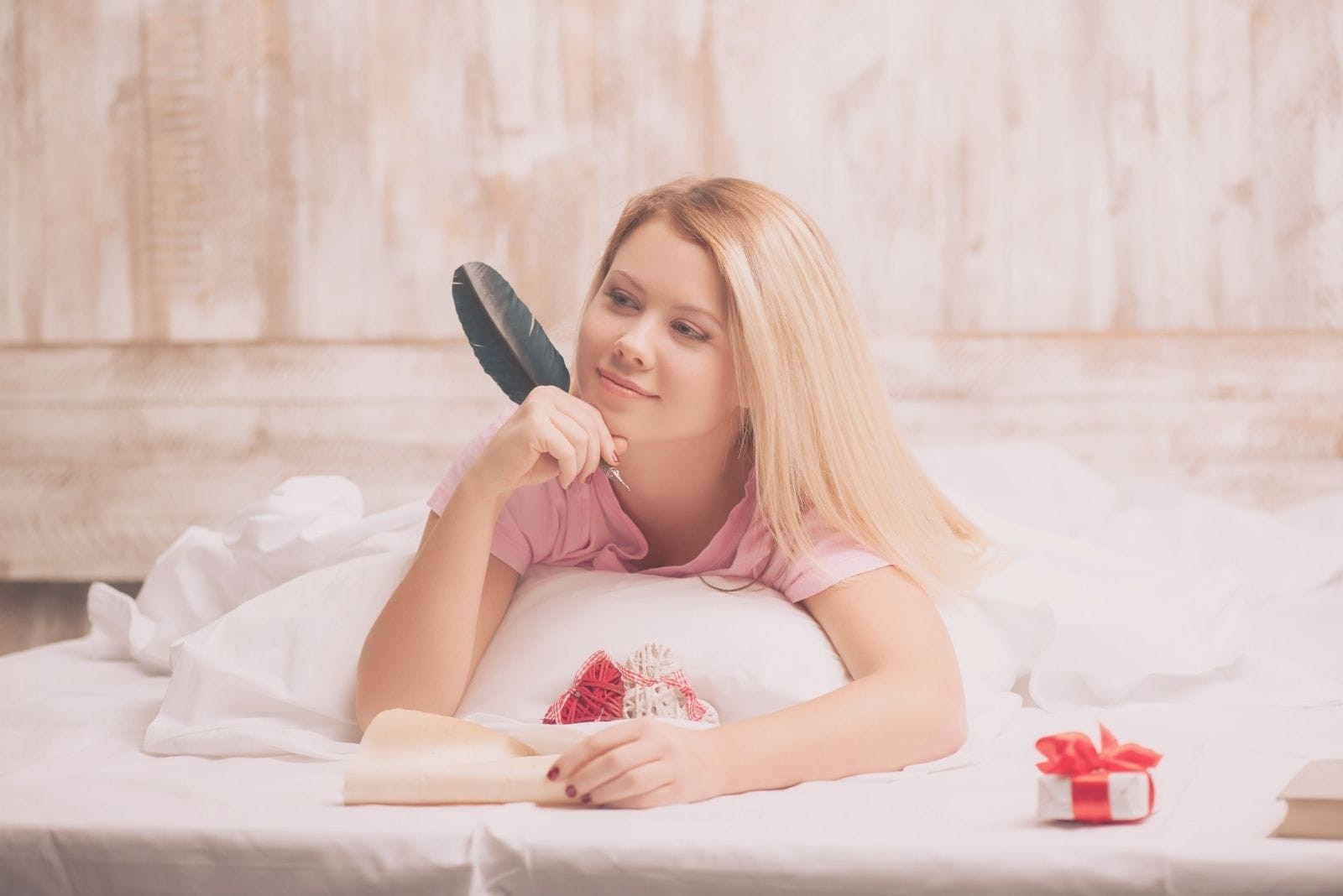 woman writing love letter in bed with a feather tip pen 