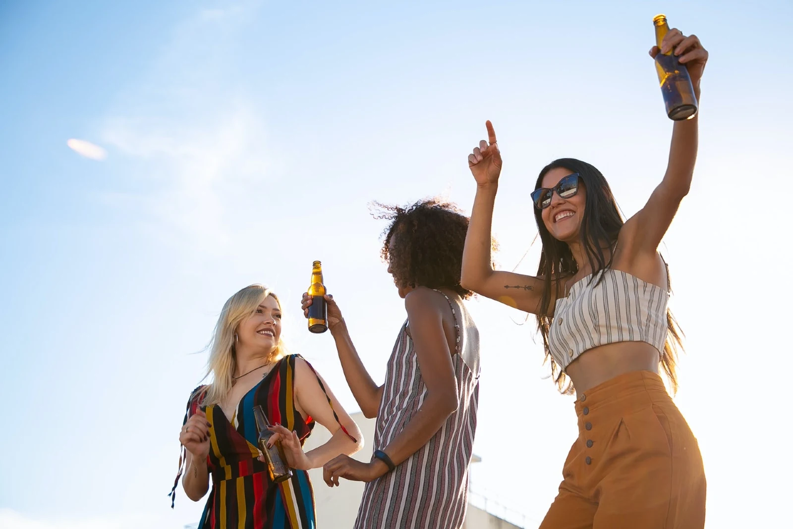 three women drinking beer while dancing on rooftop