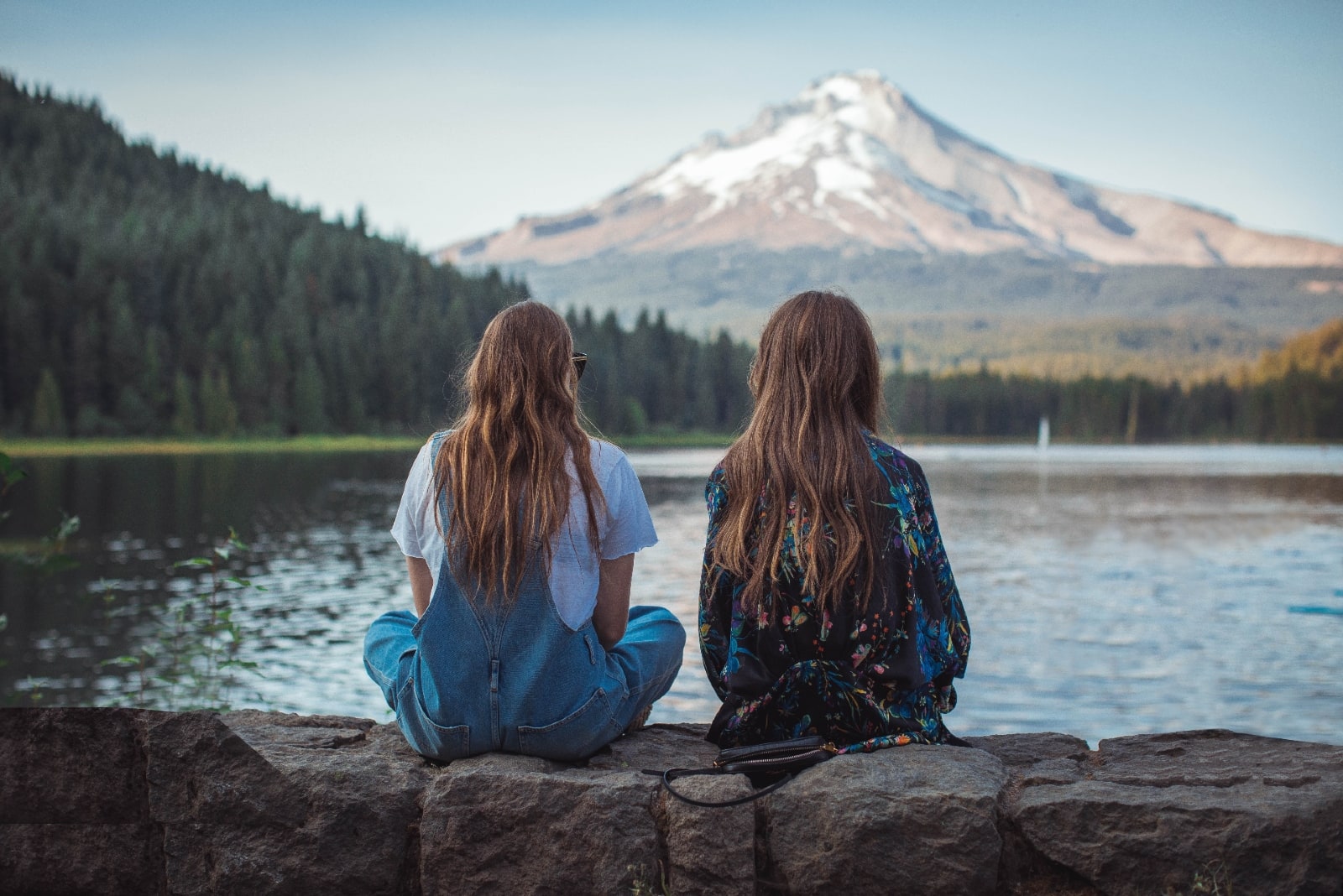 two women sitting near water looking at mountain