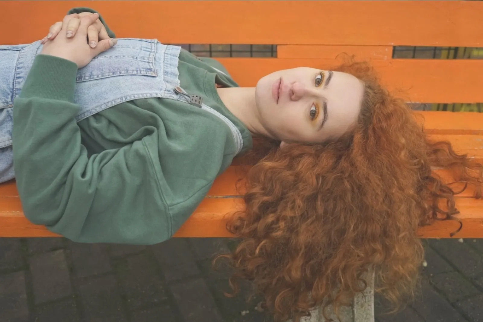 young beautiful redhead woman lying down in the park's bench 