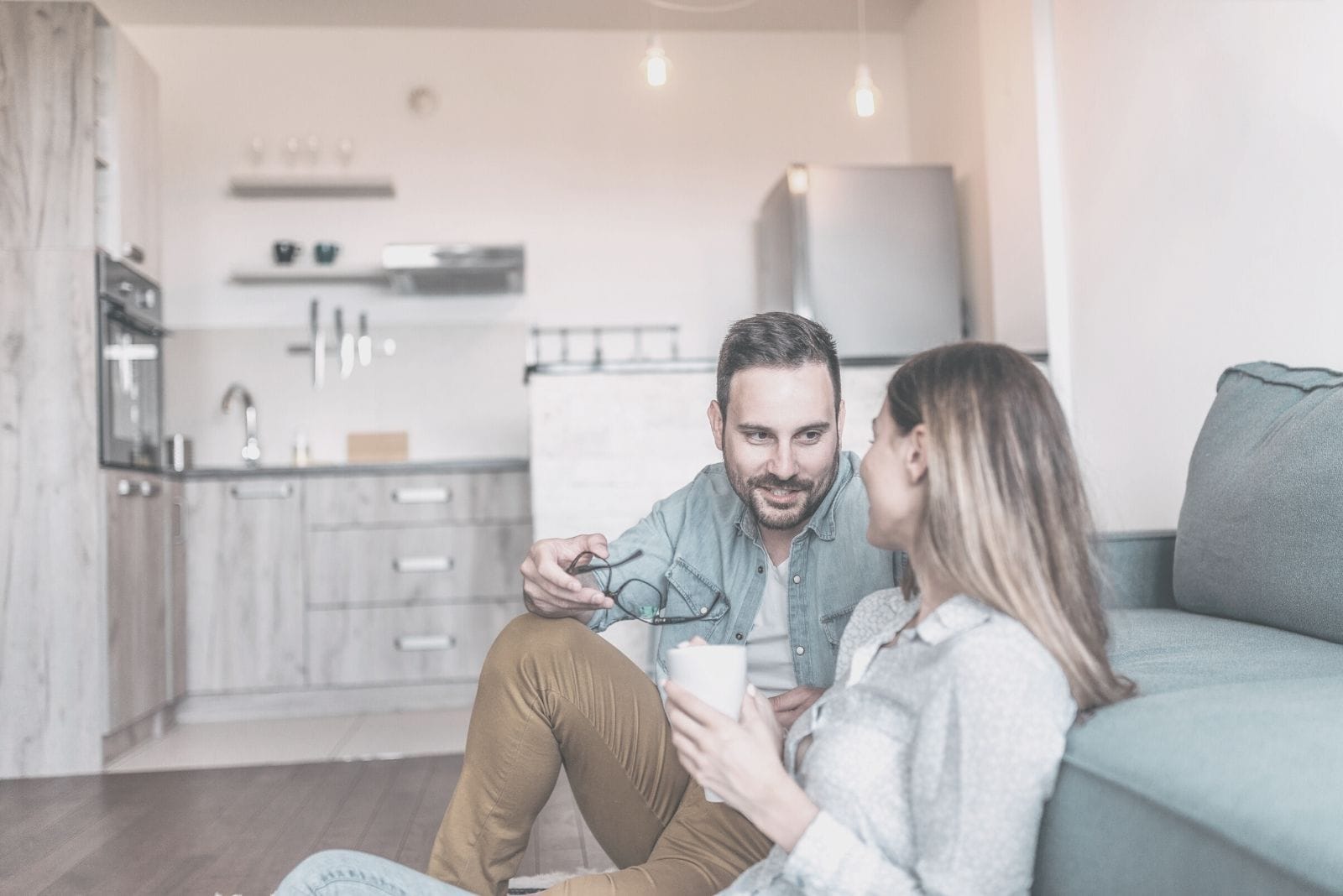 young couple squatting on the living room's floor talking and leaning on the sofa