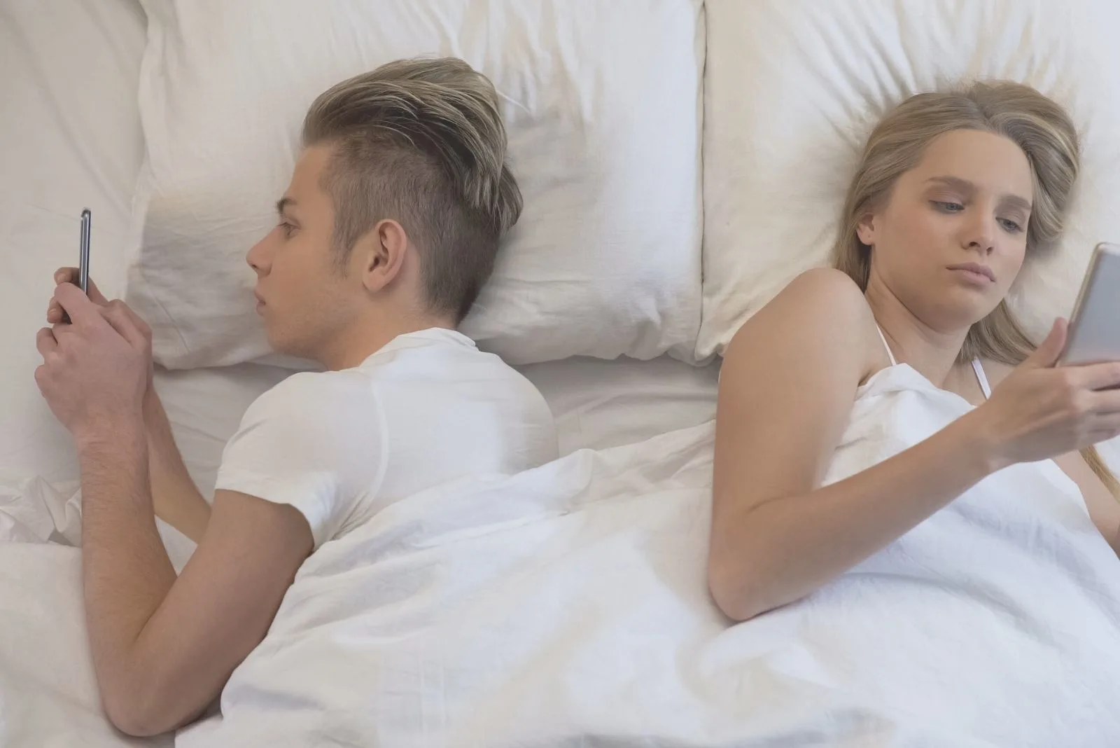 young couple surfing the net while lying down in bed back to back