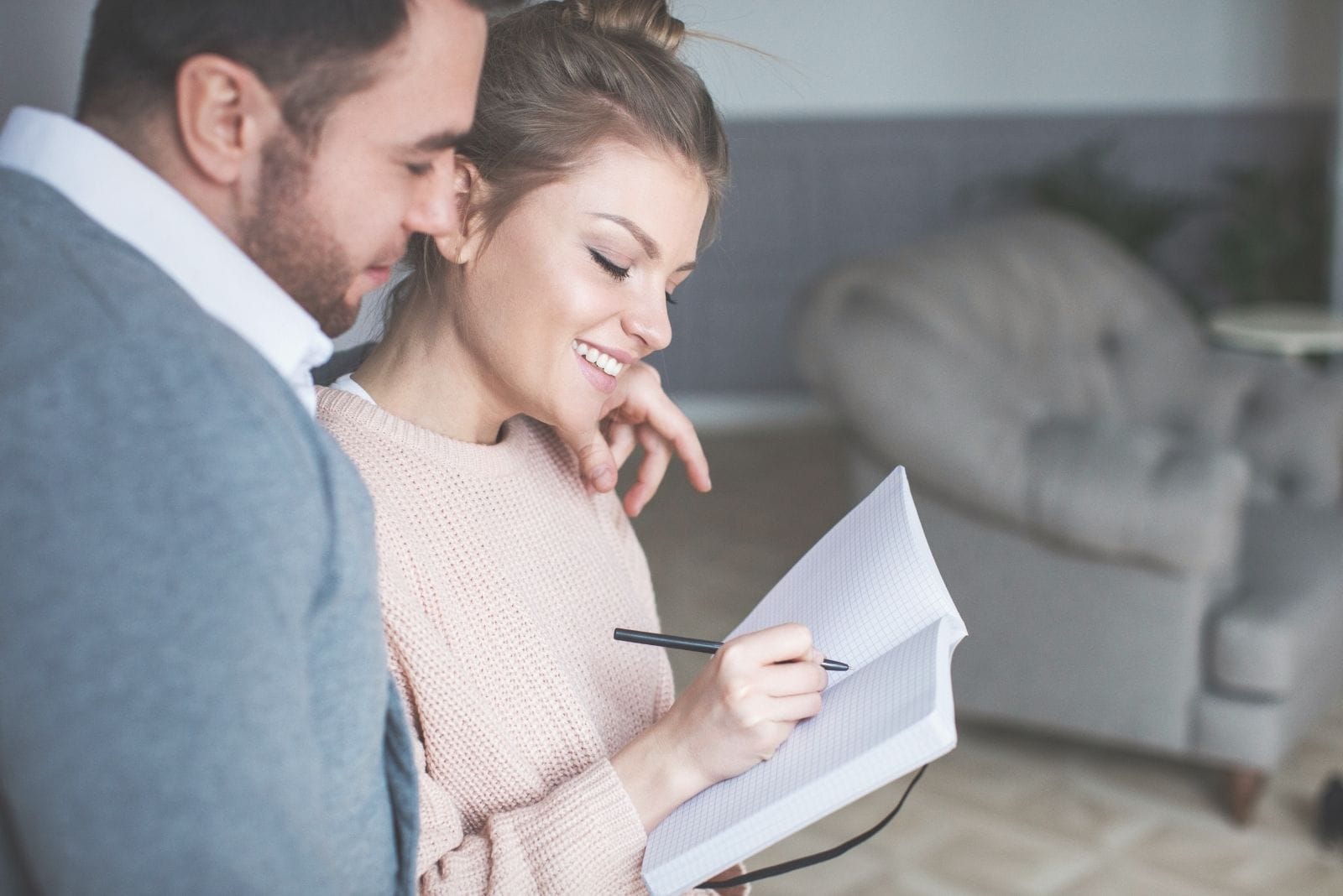 young couple writing on a notebook their future dreams while sitting inside the living room