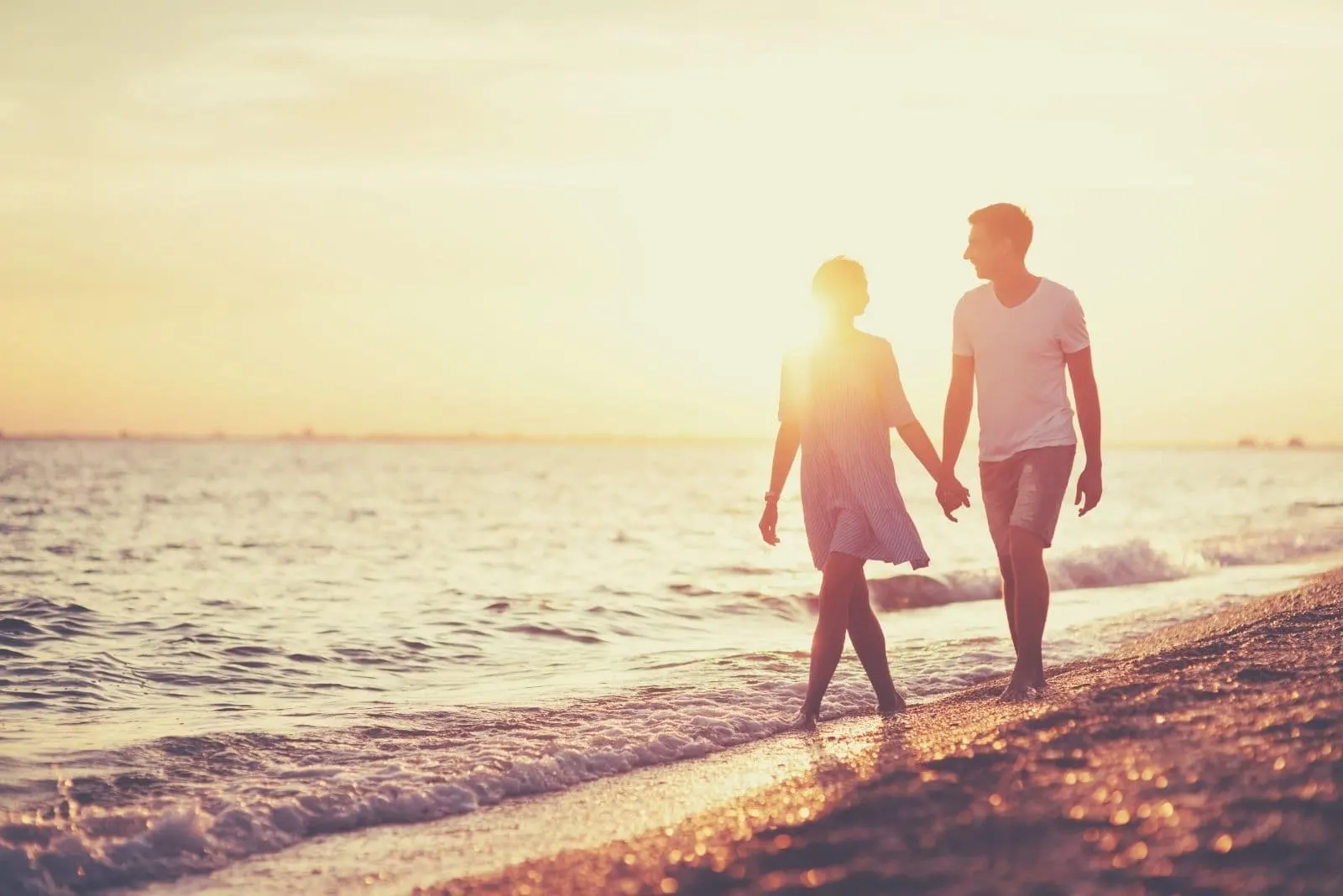 young happy couple on seashore walking while holding hands and talking