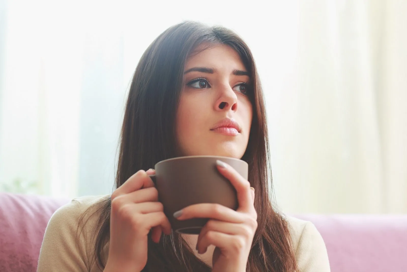 young hispanic pensive woman looking away while holding a cup of beverage
