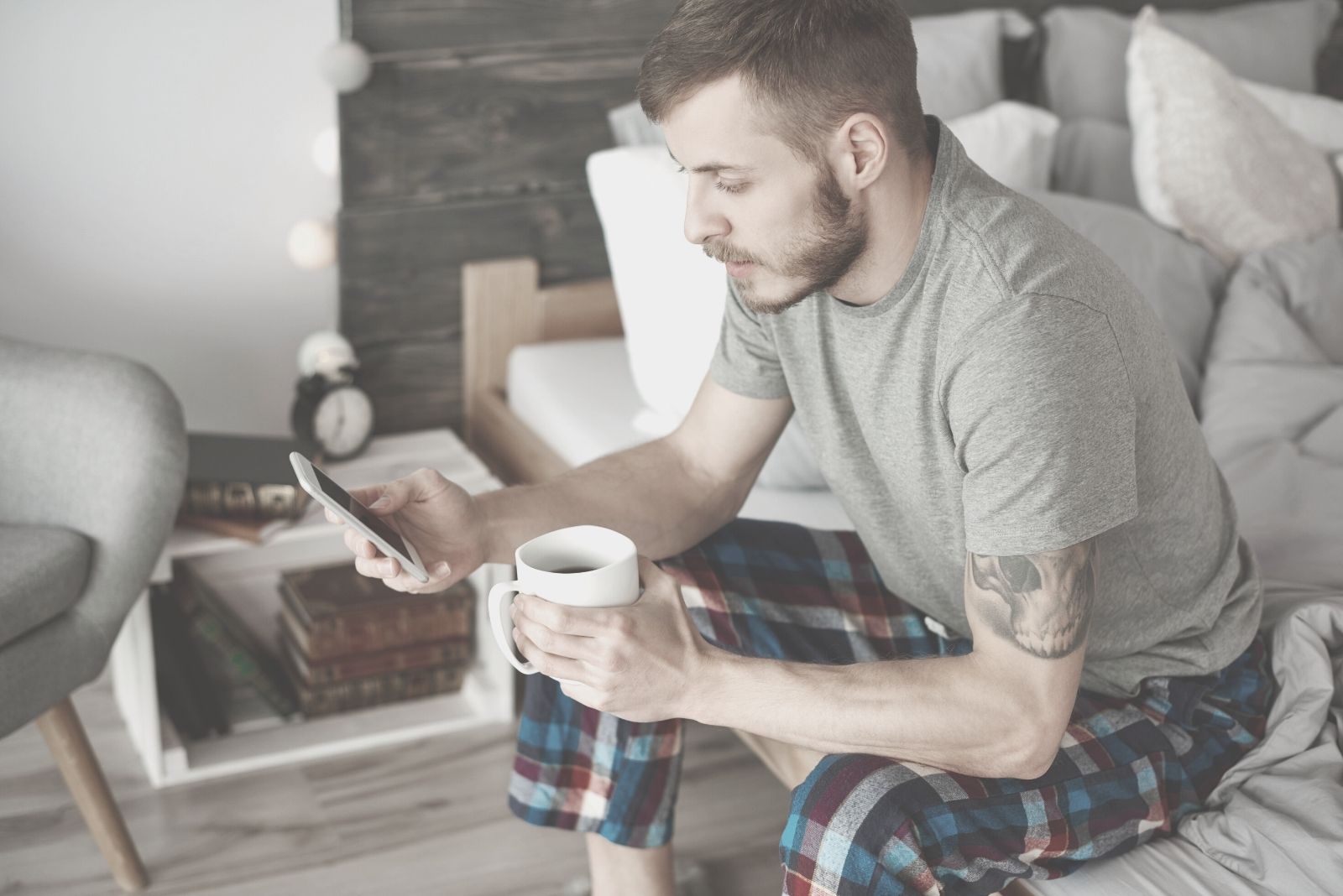 giovane uomo che beve caffè e legge un messaggio di testo all'interno della stanza