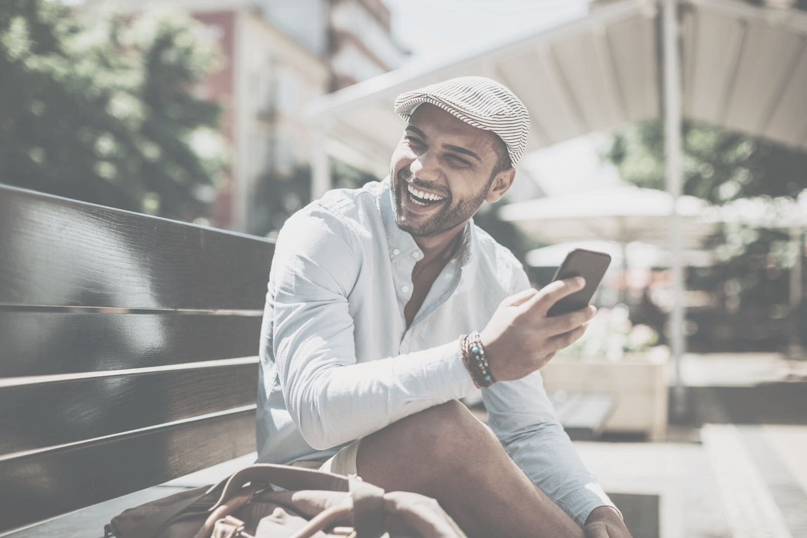 young man laughing at reading of the text message while sitting outdoors