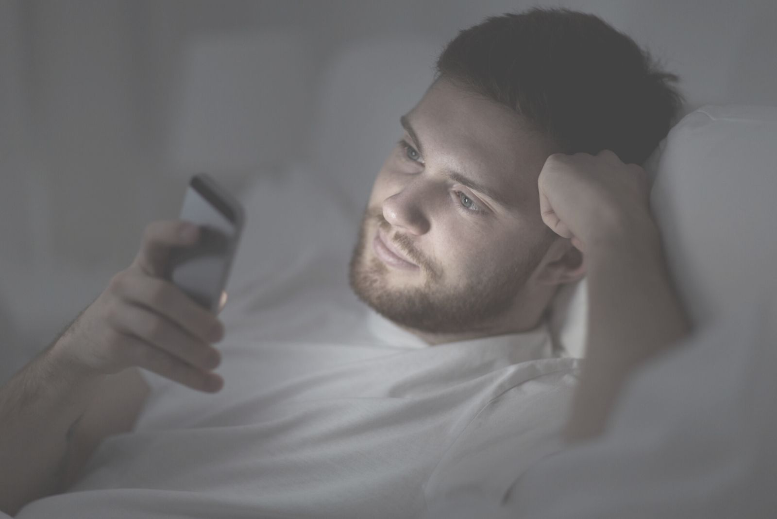giovane uomo che legge un messaggio di testo in una stanza buia, sdraiato a letto
