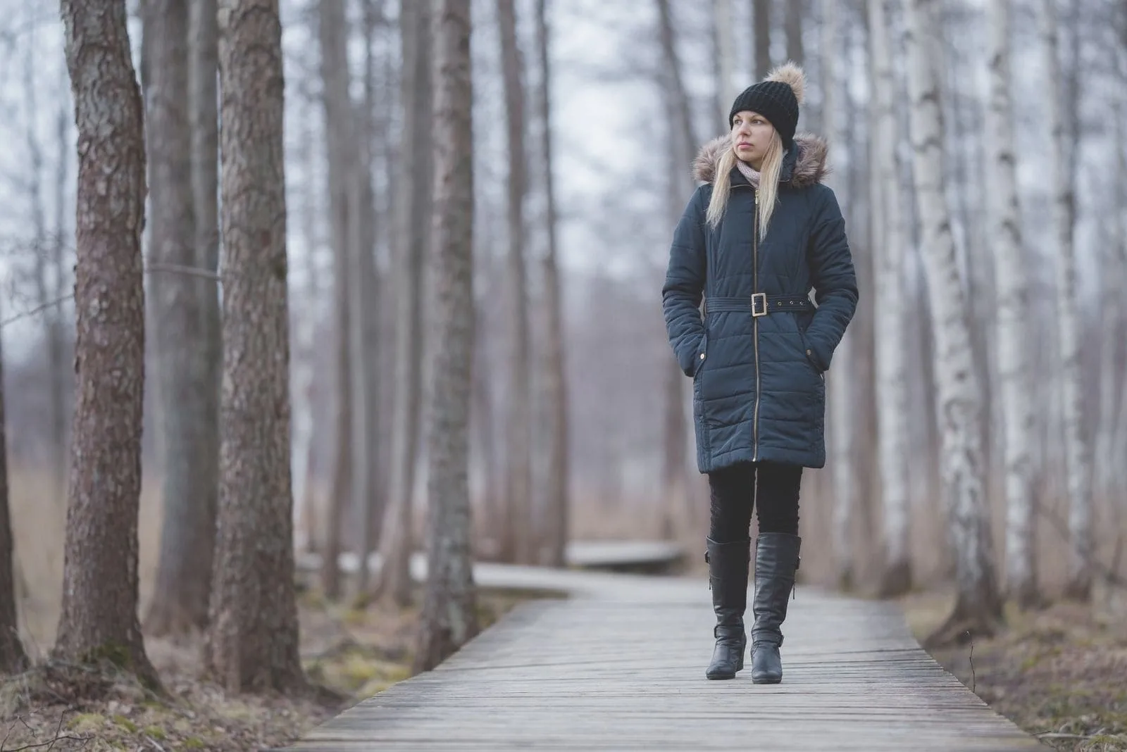 young woman in dark warm clothes walking in wooden trail of a peaceful park