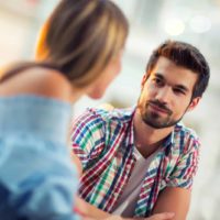 homem feliz a olhar para uma mulher enquanto está sentado à mesa