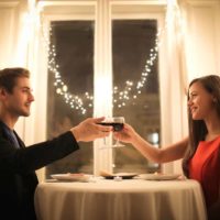 man and woman toasting wine glasses while sitting at table
