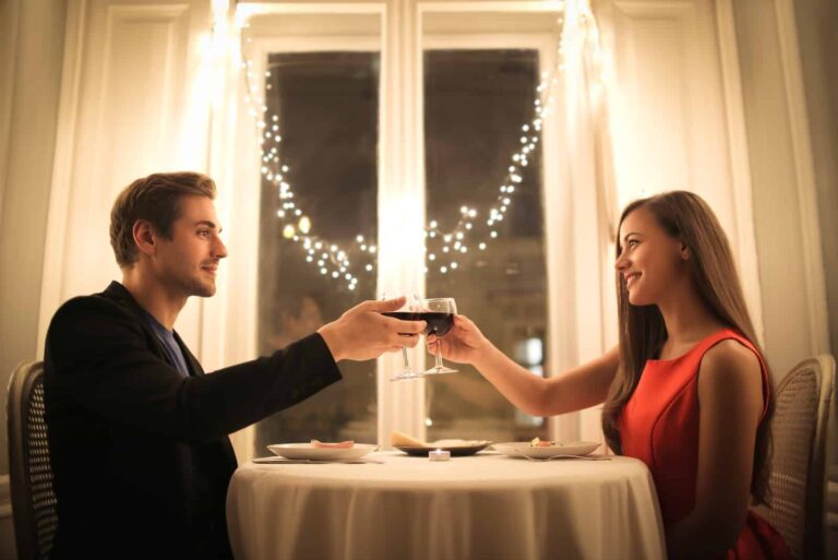 man and woman toasting wine glasses while sitting at table