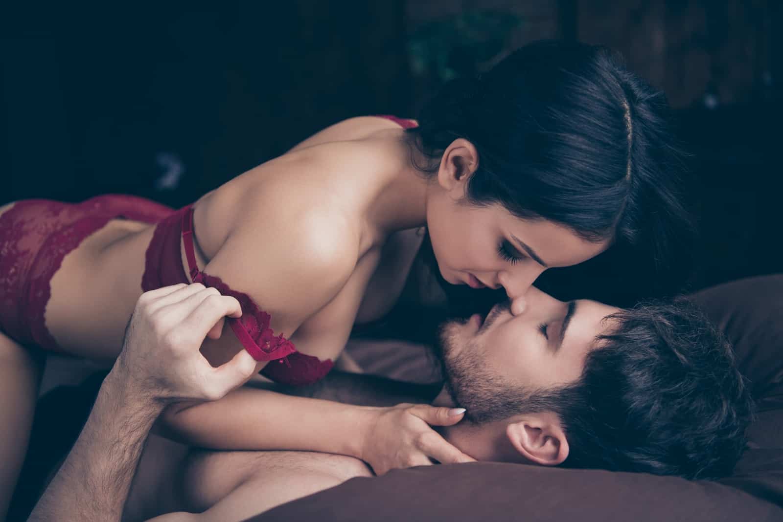 woman in red bra about to kiss man while laying on bed