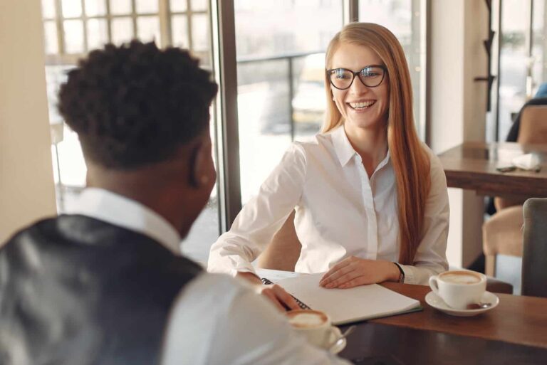 happy woman in white shirt looking at man while sitting in cafe