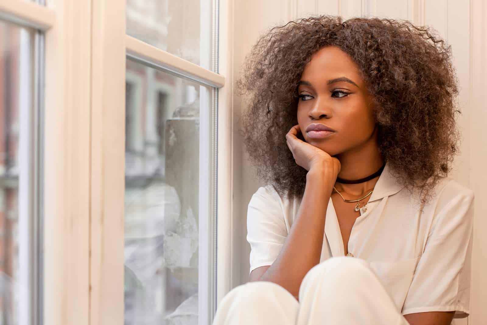 pensive woman with curly hair sitting near window