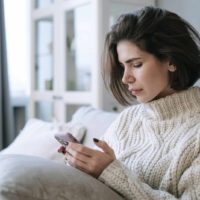 woman looking at smartphone sitting on sofa